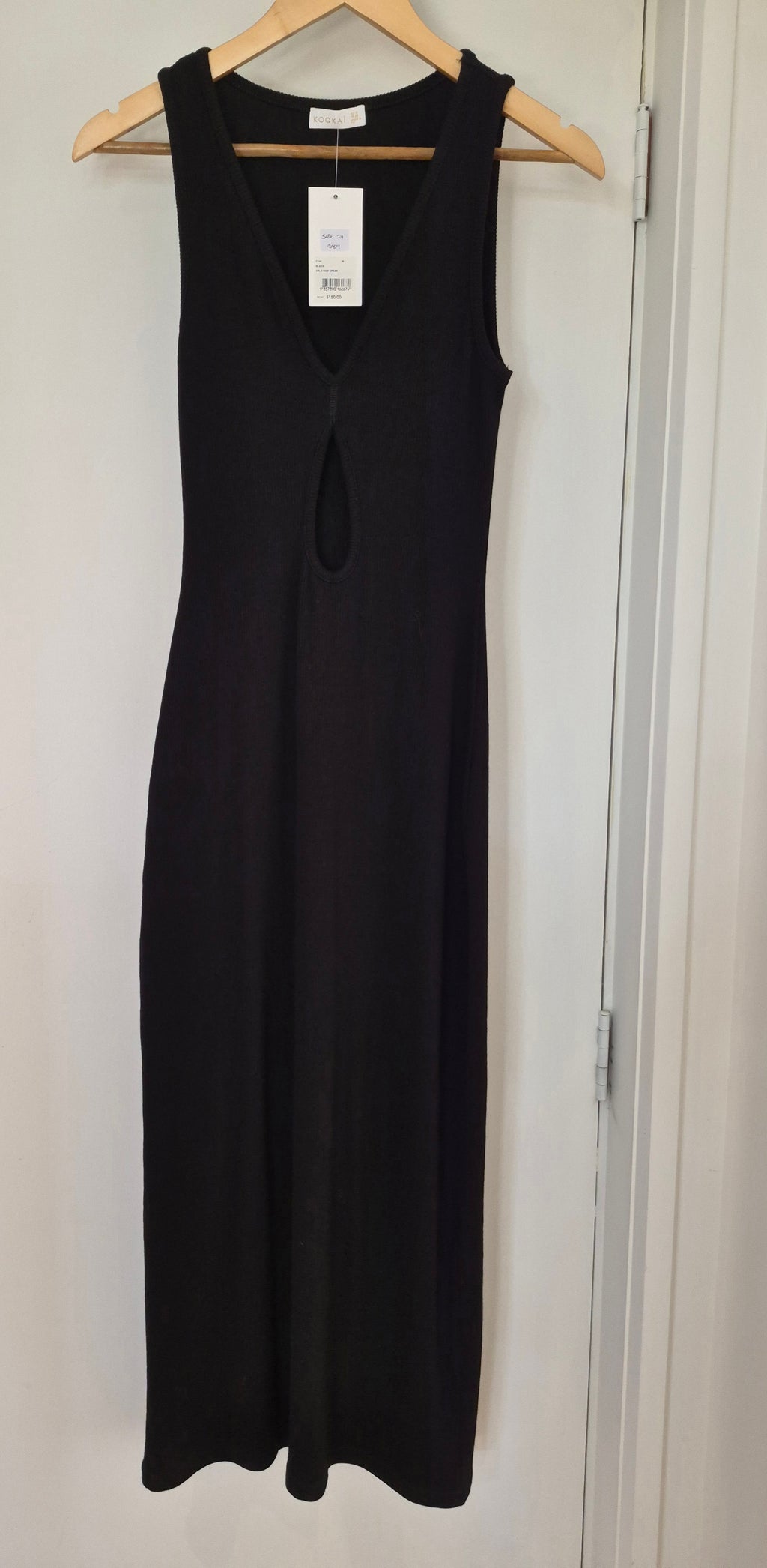 Black sleeveless Kookai dress on a hanger against a white wall